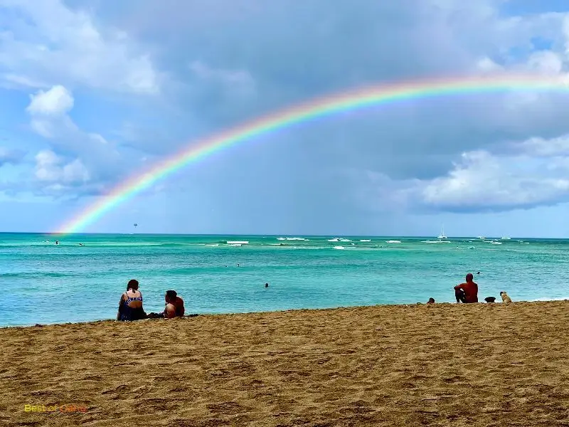 Moana Surfrider beachfront with a bright rainbow rising in the distance from the ocean.