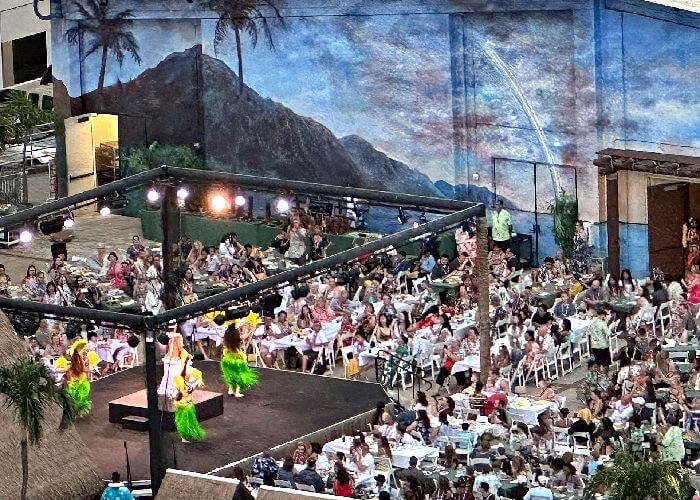 Waikiki Starlight Luau Waikiki Starlight Luau on the garage rooftop at the Hilton Hawaiian Village. Hula dancers performing for guests in attendance and a huge Diamond Head mural painting in the background.